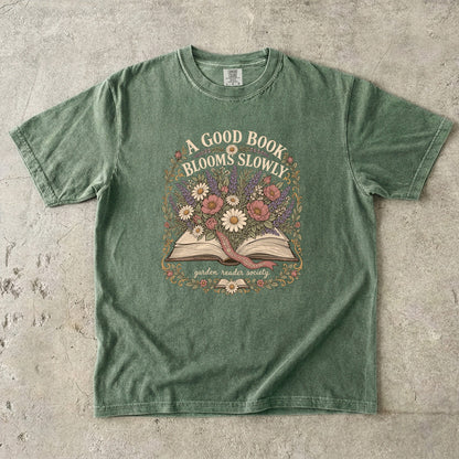 A Good Book Blooms Slowly botanical reading T-shirt with an open book and flowers on Moss.