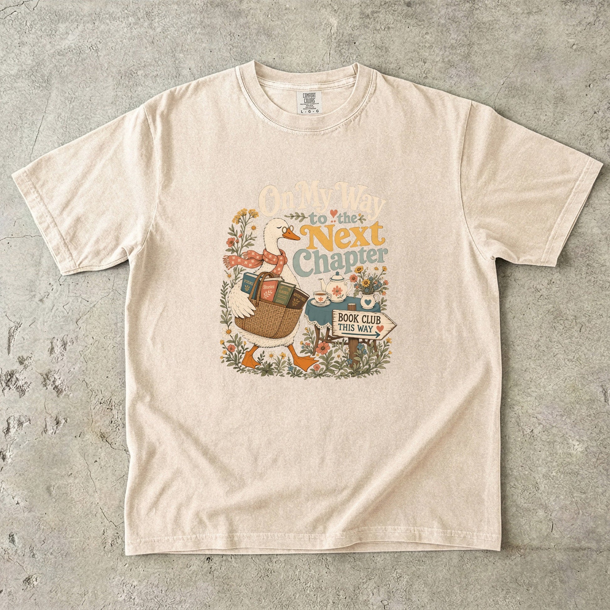On My Way to the Next Chapter book club T-shirt with goose carrying a basket of books on Ivory.