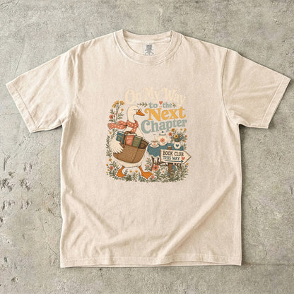 On My Way to the Next Chapter book club T-shirt with goose carrying a basket of books on Ivory.