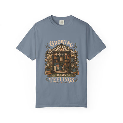 Growing a Library of Feelings book lover T-shirt in Blue Jean featuring a botanical greenhouse library with books and a reading chair
