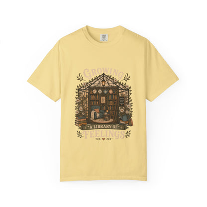 Growing a Library of Feelings book lover T-shirt in Butter featuring a botanical greenhouse library with books and a reading chair