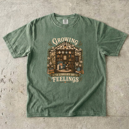 Growing a Library of Feelings book lover T-shirt in moss featuring a botanical greenhouse library with books and a reading chair
