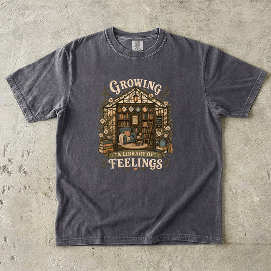 Growing a Library of Feelings book lover T-shirt in Pepper featuring a botanical greenhouse library with books and a reading chair
