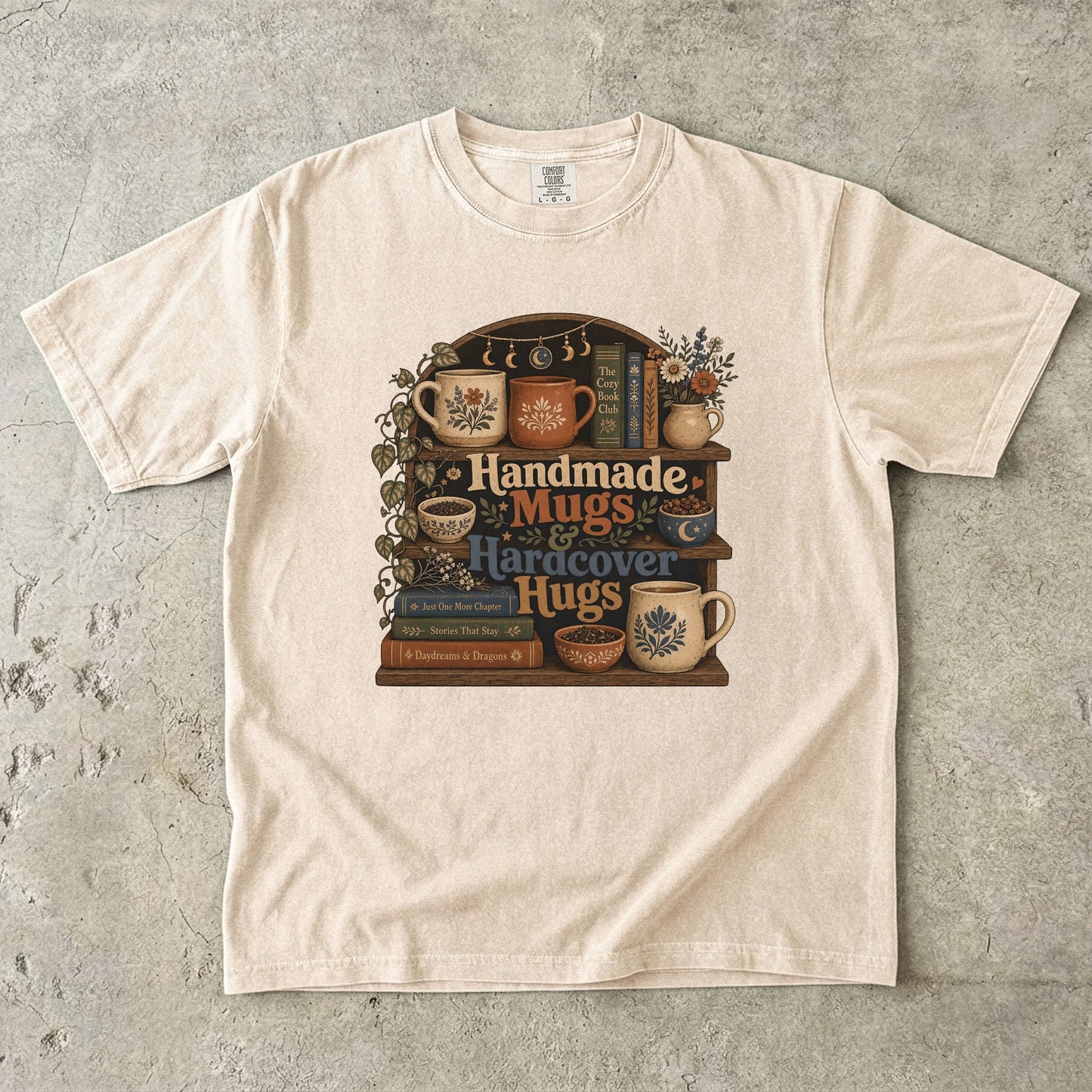 Front view of an Ivory Comfort Colors book lover shirt featuring handmade mugs, bookshelves and vintage cottagecore book artwork.