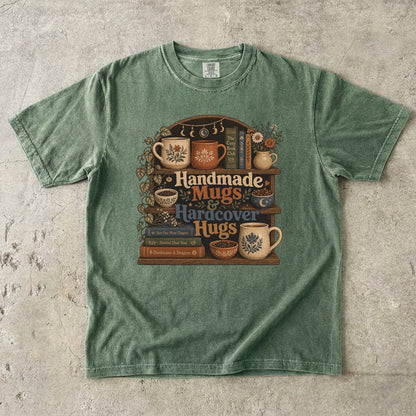 Front view of a Moss Comfort Colors book lover shirt featuring handcrafted mugs, hardcover books and botanical bookshelf illustration.