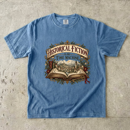 Blue Jean T-shirt featuring “Historical Fiction Is My Time Machine” with an open book revealing an old-world town, ornate gold framing, antique books, leaves and burgundy flowers.