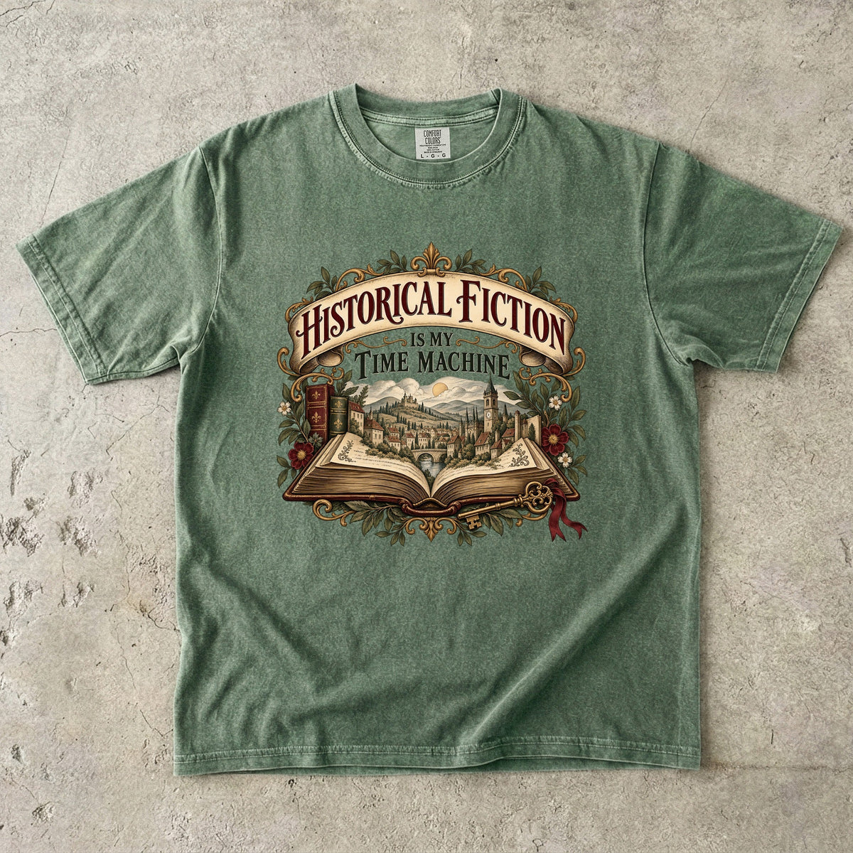 Moss T-shirt featuring “Historical Fiction Is My Time Machine” with an open book revealing an old-world town, ornate gold framing, antique books, leaves and burgundy flowers.