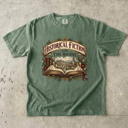 Moss T-shirt featuring “Historical Fiction Is My Time Machine” with an open book revealing an old-world town, ornate gold framing, antique books, leaves and burgundy flowers.