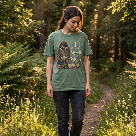 Woman wearing the I Found Myself In A Story Book Lover Shirt while walking through a peaceful woodland, featuring a vintage literary design with an antique mirror and moonlit cottage.