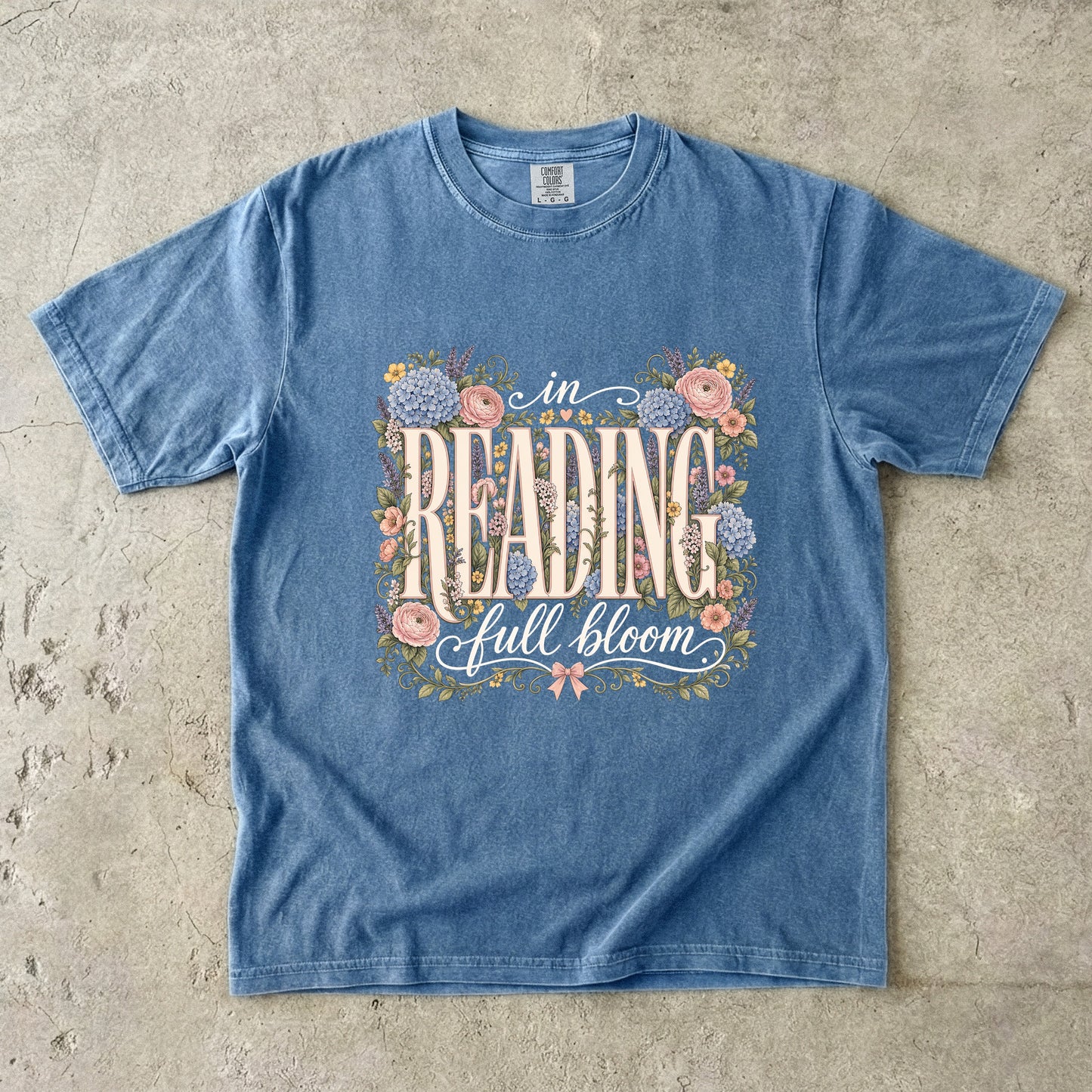 Blue Jean Comfort Colors reading T-shirt featuring the floral In Reading, Full Bloom book lover design with pink and blue flowers.