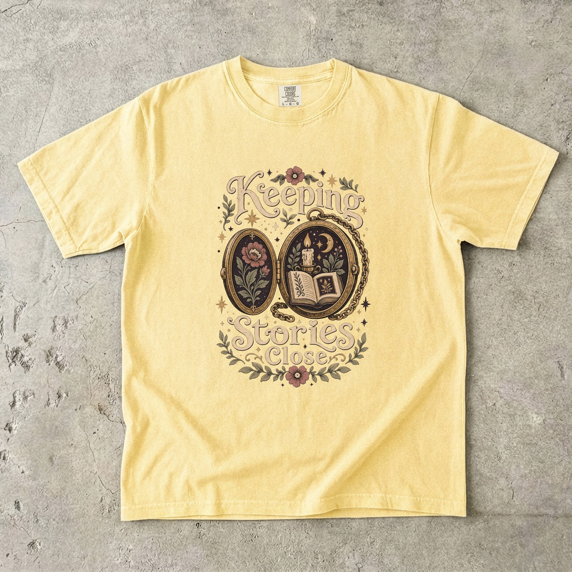 Front view of a Butter Comfort Colors Book Lover T-shirt with the Keeping Stories Close illustration.