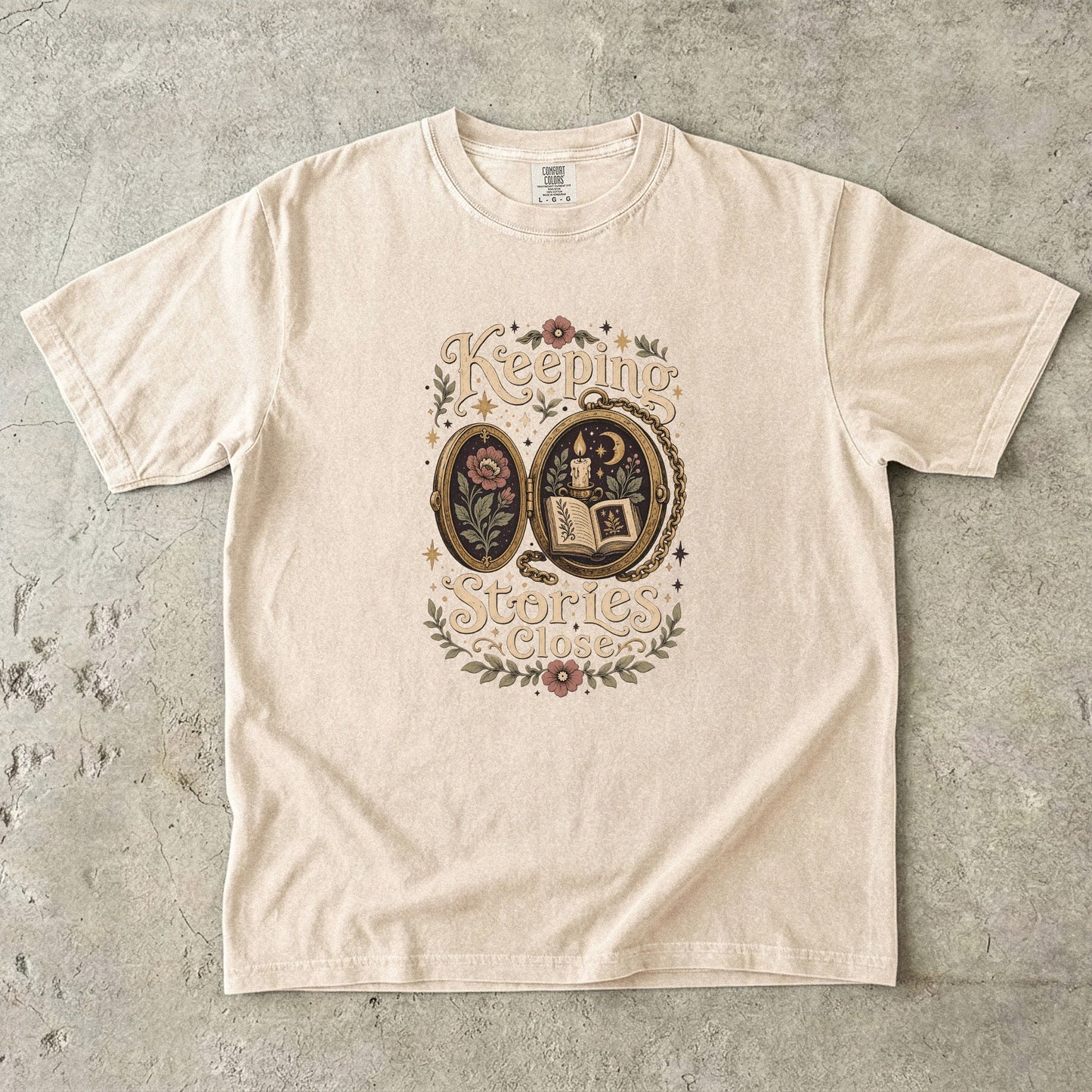 Front view of an Ivory Comfort Colors Book Lover T-shirt featuring the Keeping Stories Close vintage literary locket illustration.