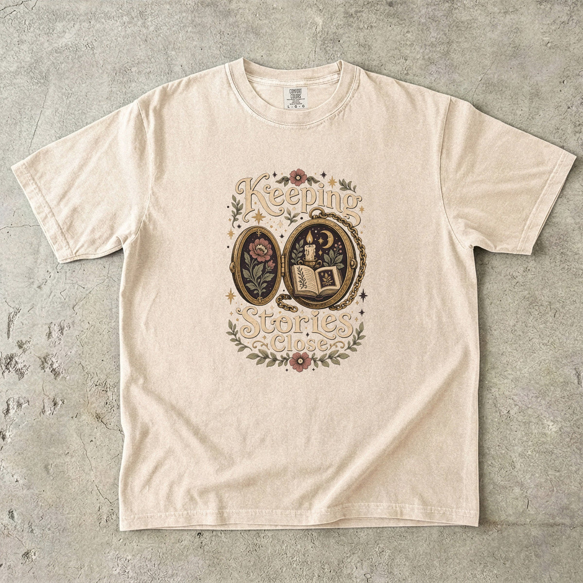 Keeping Stories Close book lover T-shirt in Ivory featuring an ornate locket with an open book, candle, moon and flowers