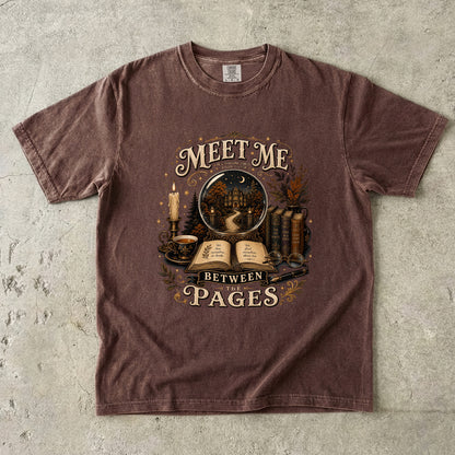 Meet Me Between the Pages book lover Comfort Colors T-shirt in Espresso with vintage books, candle and fictional world illustration.