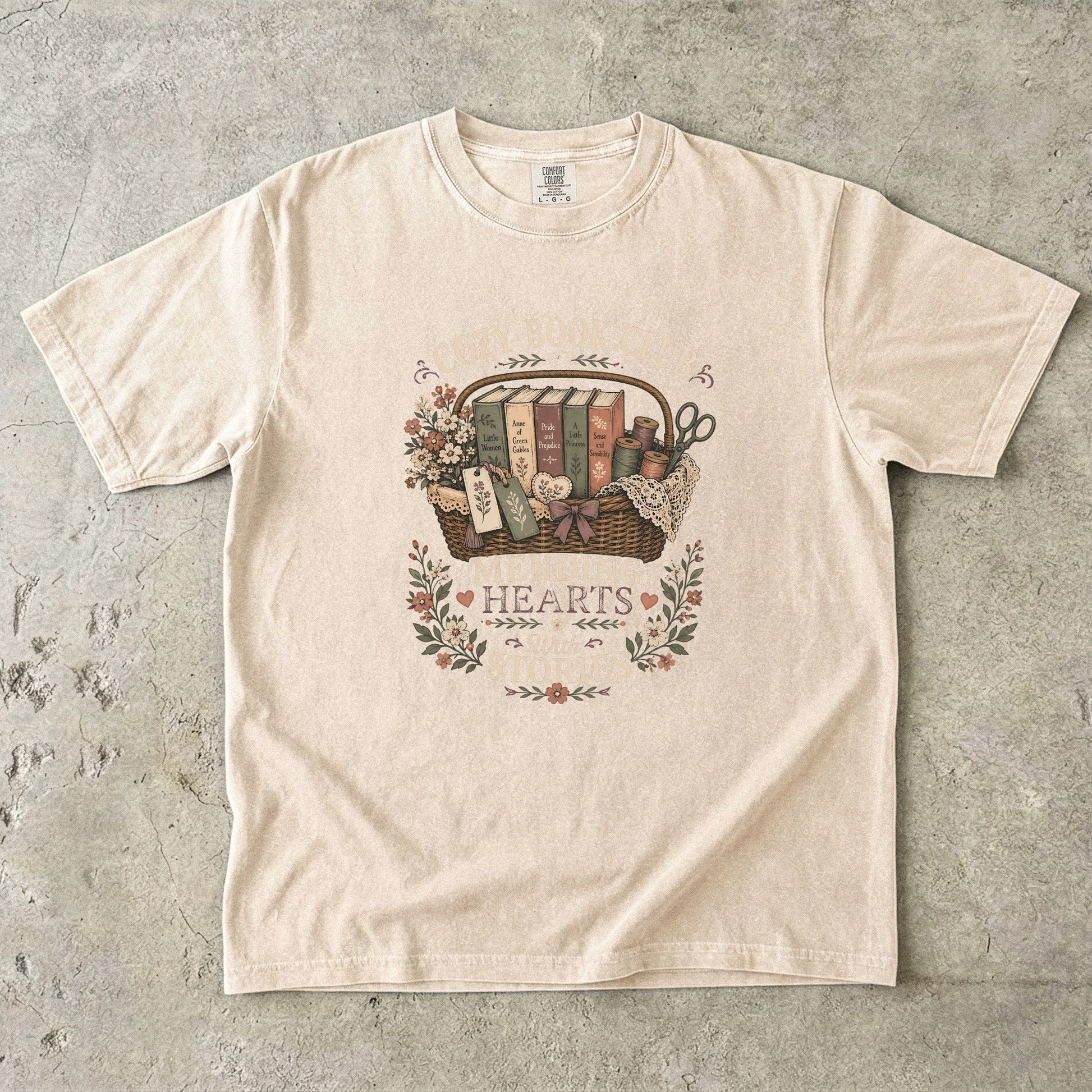 Mending Hearts With Stories book club T-shirt in Ivory featuring classic books, sewing notions, flowers and a woven basket
