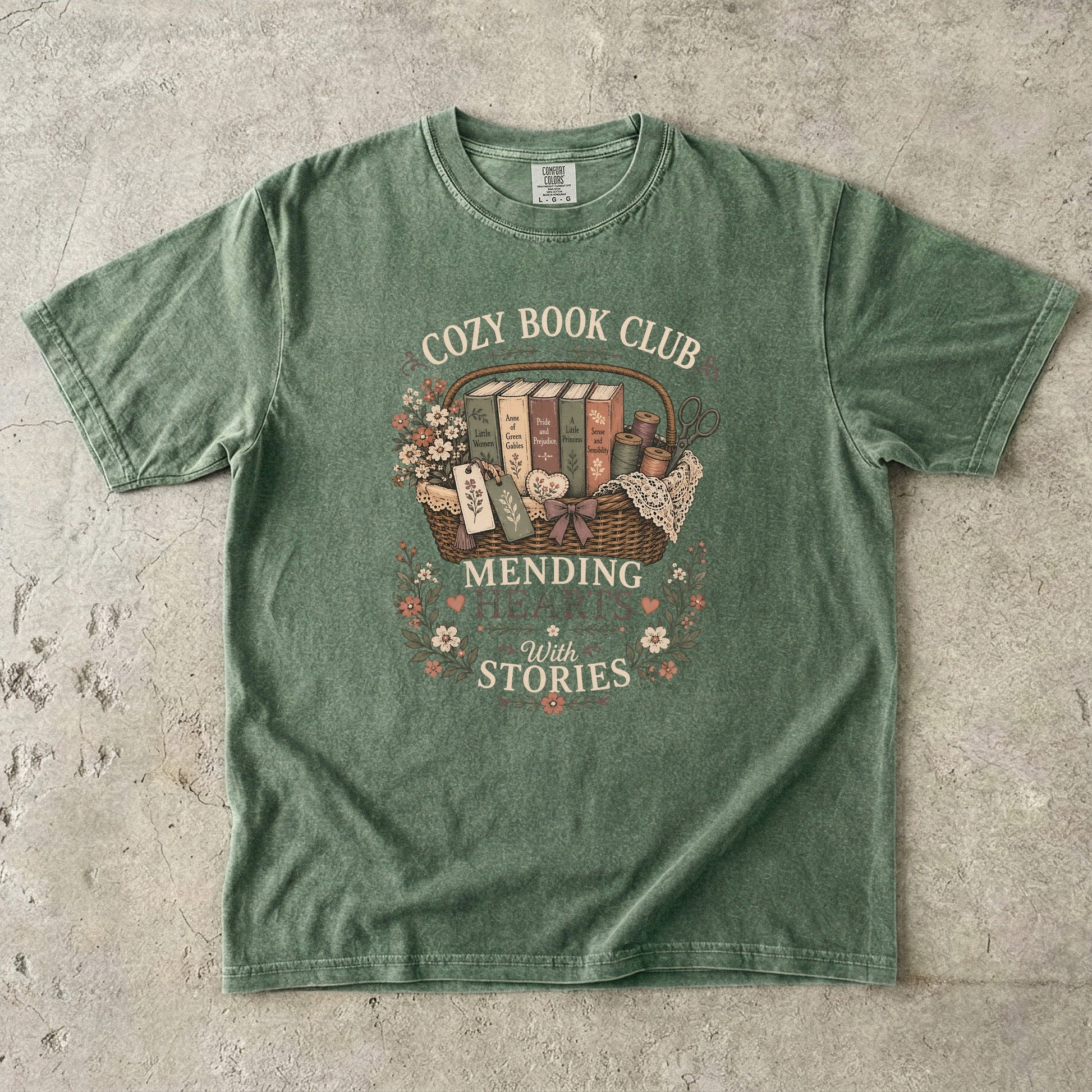 Mending Hearts With Stories book club T-shirt in Moss featuring classic books, sewing notions, flowers and a woven basket