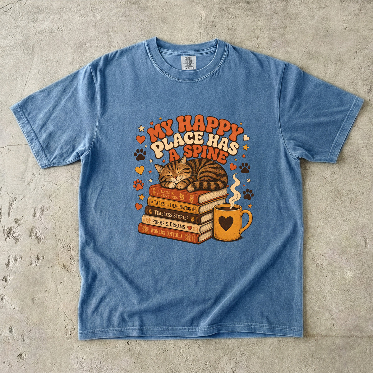 Blue Jean cat book lover T-shirt featuring a sleeping tabby on stacked books beside a steaming mug with hearts, stars and paw prints.