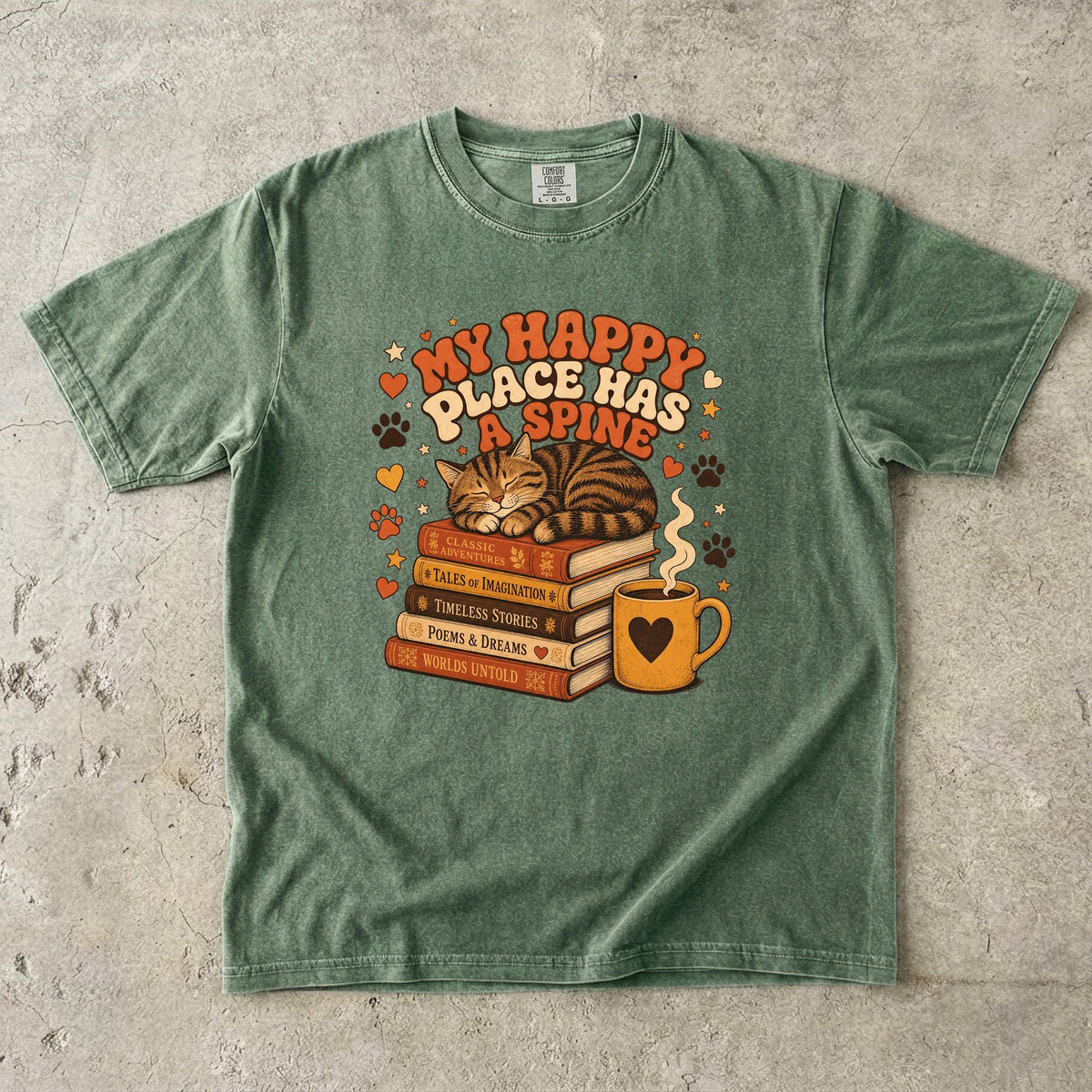 Moss cat book lover T-shirt featuring a sleeping tabby on stacked books beside a steaming mug with hearts, stars and paw prints.
