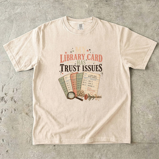 Ivory library lover T-shirt featuring My Library Card Has Trust Issues with vintage library checkout cards, flowers and a magnifying glass.