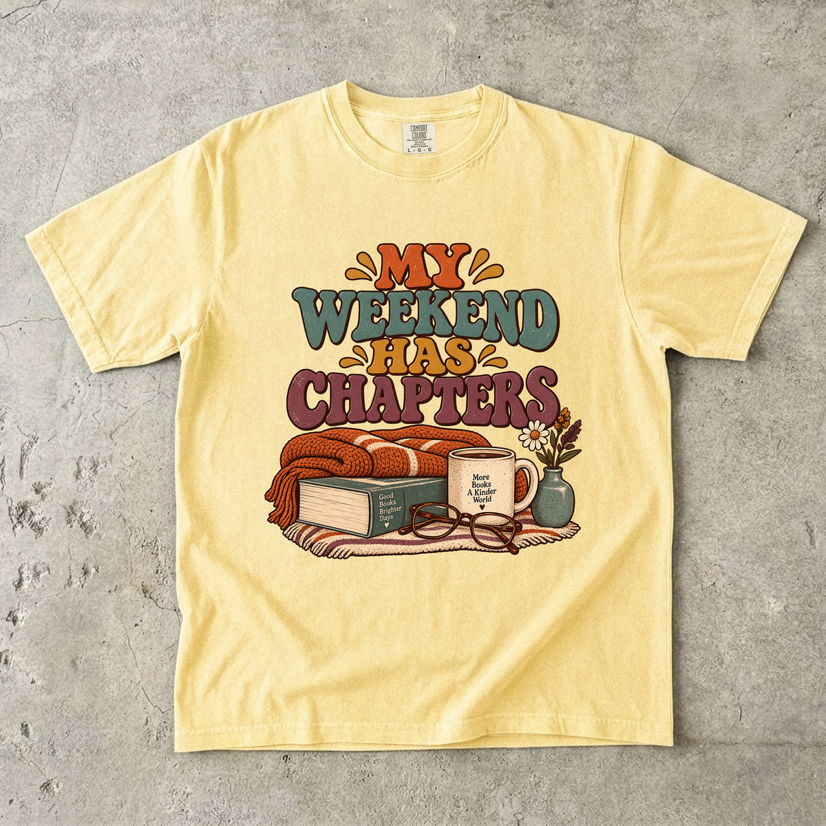 Butter T-shirt featuring “My Weekend Has Chapters” with multicolored vintage lettering, a knitted blanket, book, mug, glasses and a small flower vase.