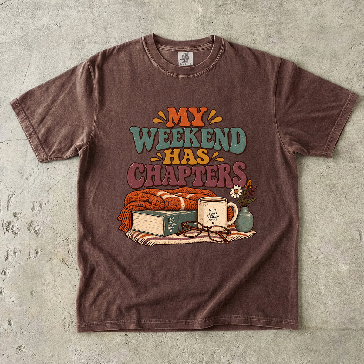 Espresso T-shirt featuring “My Weekend Has Chapters” with multicolored vintage lettering, a knitted blanket, book, mug, glasses and a small flower vase.