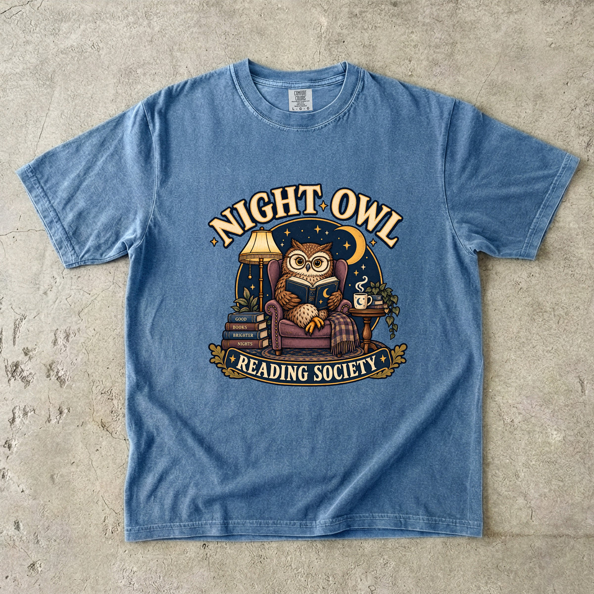 Blue Jean T-shirt featuring “Night Owl Reading Society” with a spectacled owl reading in an armchair, a lamp, books, mug, crescent moon and stars.