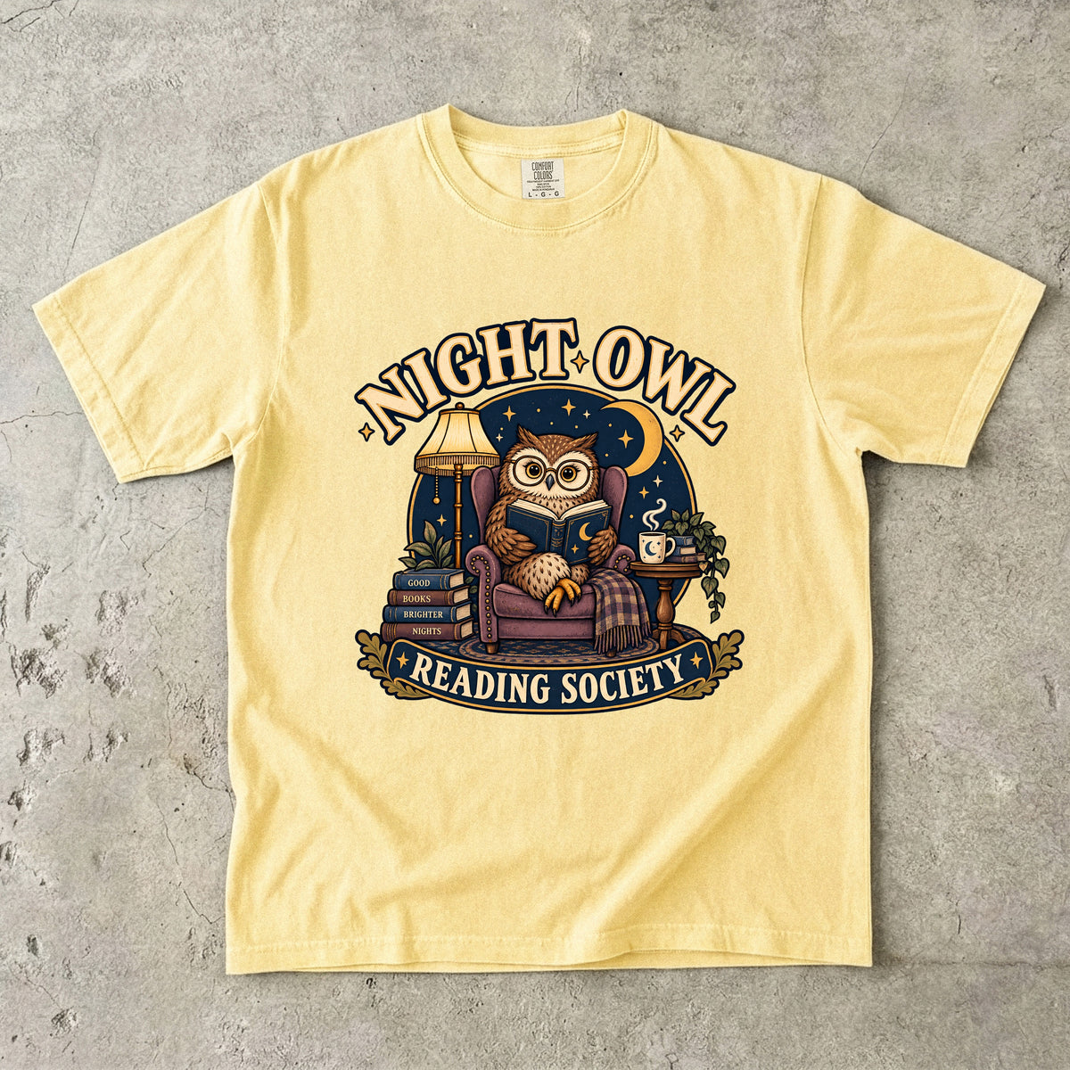 Butter T-shirt featuring “Night Owl Reading Society” with a spectacled owl reading in an armchair, a lamp, books, mug, crescent moon and stars.