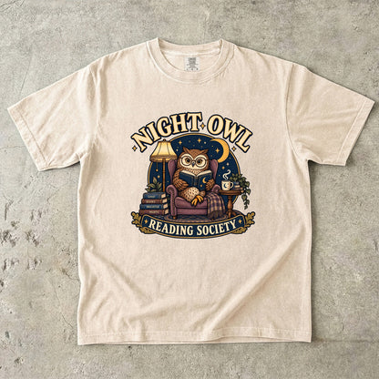 Ivory T-shirt featuring “Night Owl Reading Society” with a spectacled owl reading in an armchair, a lamp, books, mug, crescent moon and stars.