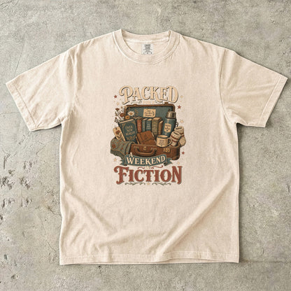 Packed for a Weekend in Fiction reading T-shirt in Ivory featuring a vintage suitcase packed with books, a mug, thermos and cozy socks