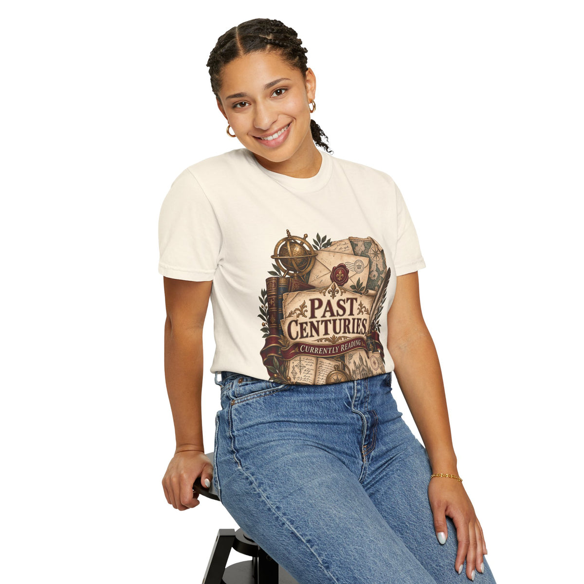 A woman wearing a cream-colored graphic t-shirt with a vintage map print that reads 'PAST CENTURIES' and blue jeans, posing against a solid white background.