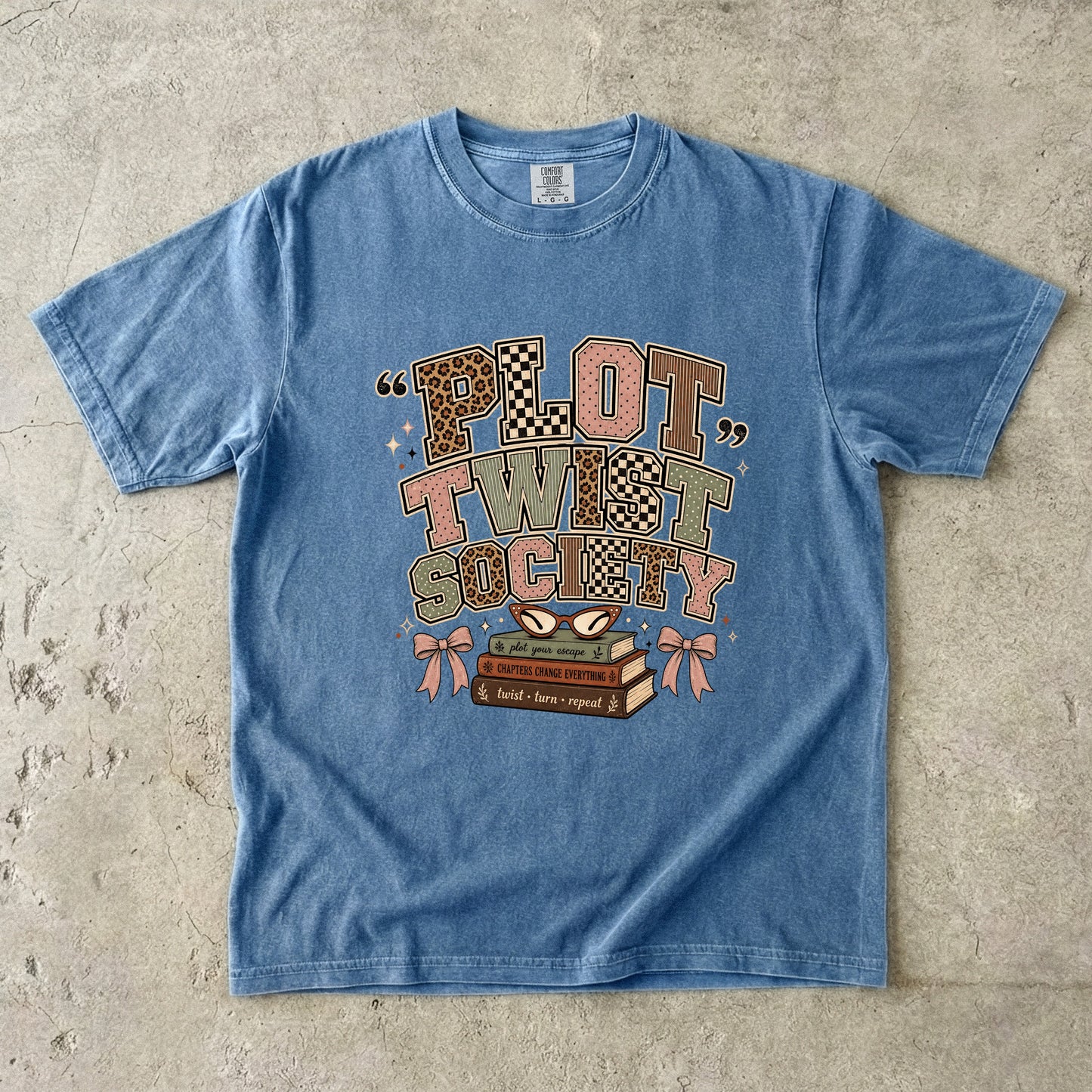 Blue Jean Comfort Colors Plot Twist Society bookish T-shirt with patterned lettering, books, glasses and bow details.