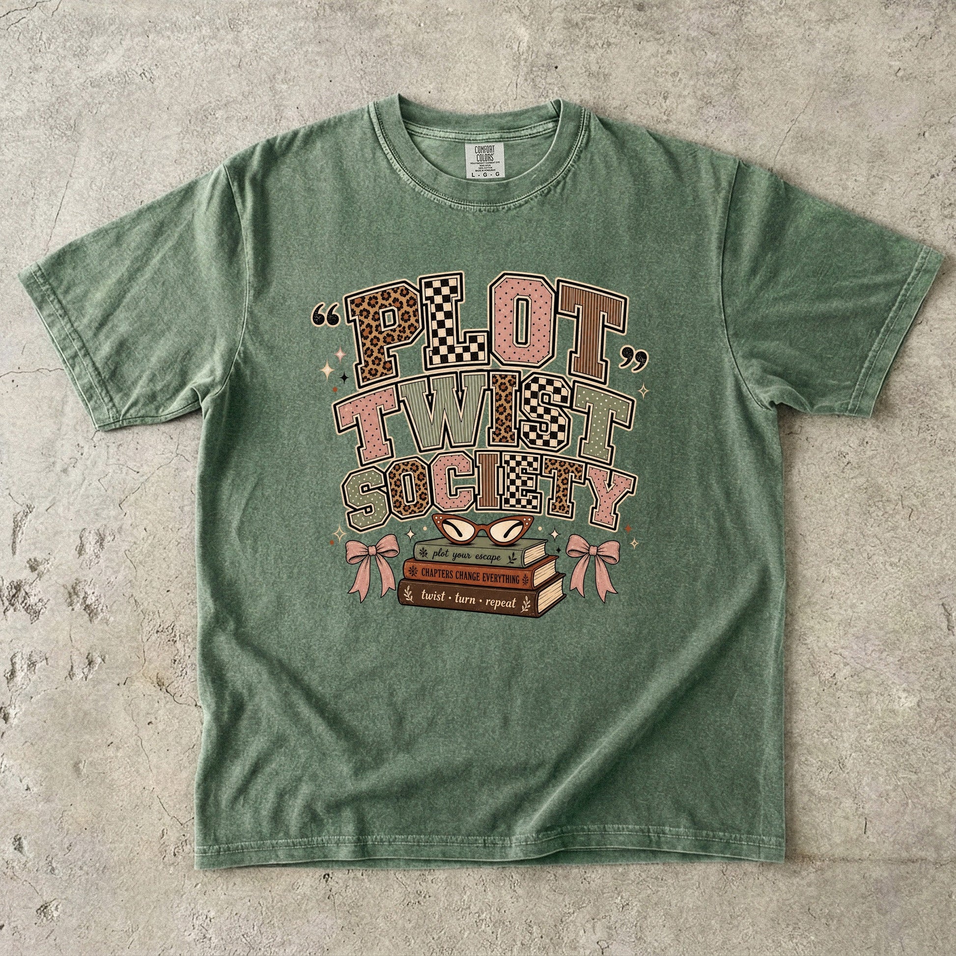 Moss Comfort Colors book lover T-shirt featuring the retro Plot Twist Society graphic with stacked books and glasses.