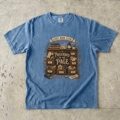 Prescribed by the Page cozy book club T-shirt in Blue Jean featuring a vintage literary cabinet filled with books, tea and reading-themed drawers