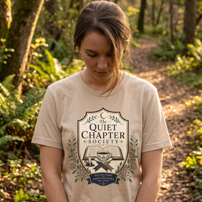 Woman wearing The Quiet Chapter Society book lover T-shirt outdoors, featuring an open book, teacup, candle and botanical design.