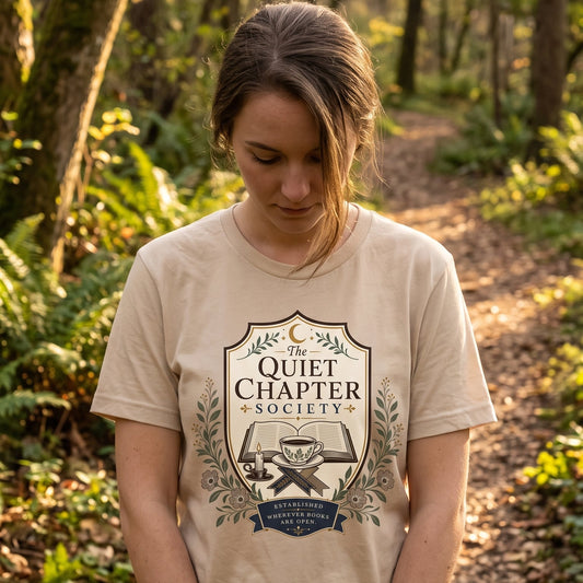 Woman wearing The Quiet Chapter Society book lover T-shirt outdoors, featuring an open book, teacup, candle and botanical design.