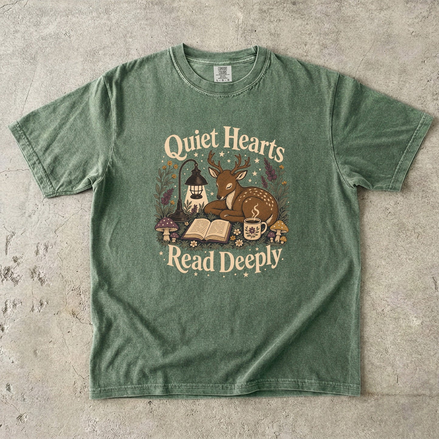 Front view of the Moss Comfort Colors® Book Lover T-shirt featuring the Quiet Hearts Read Deeply design with a woodland deer, open book, lantern and tea.