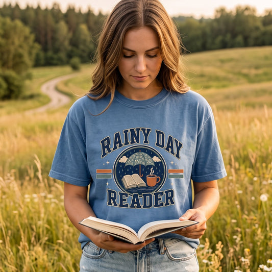 Woman reading a book outdoors wearing a Blue Jean Rainy Day Reader book lover T-shirt.