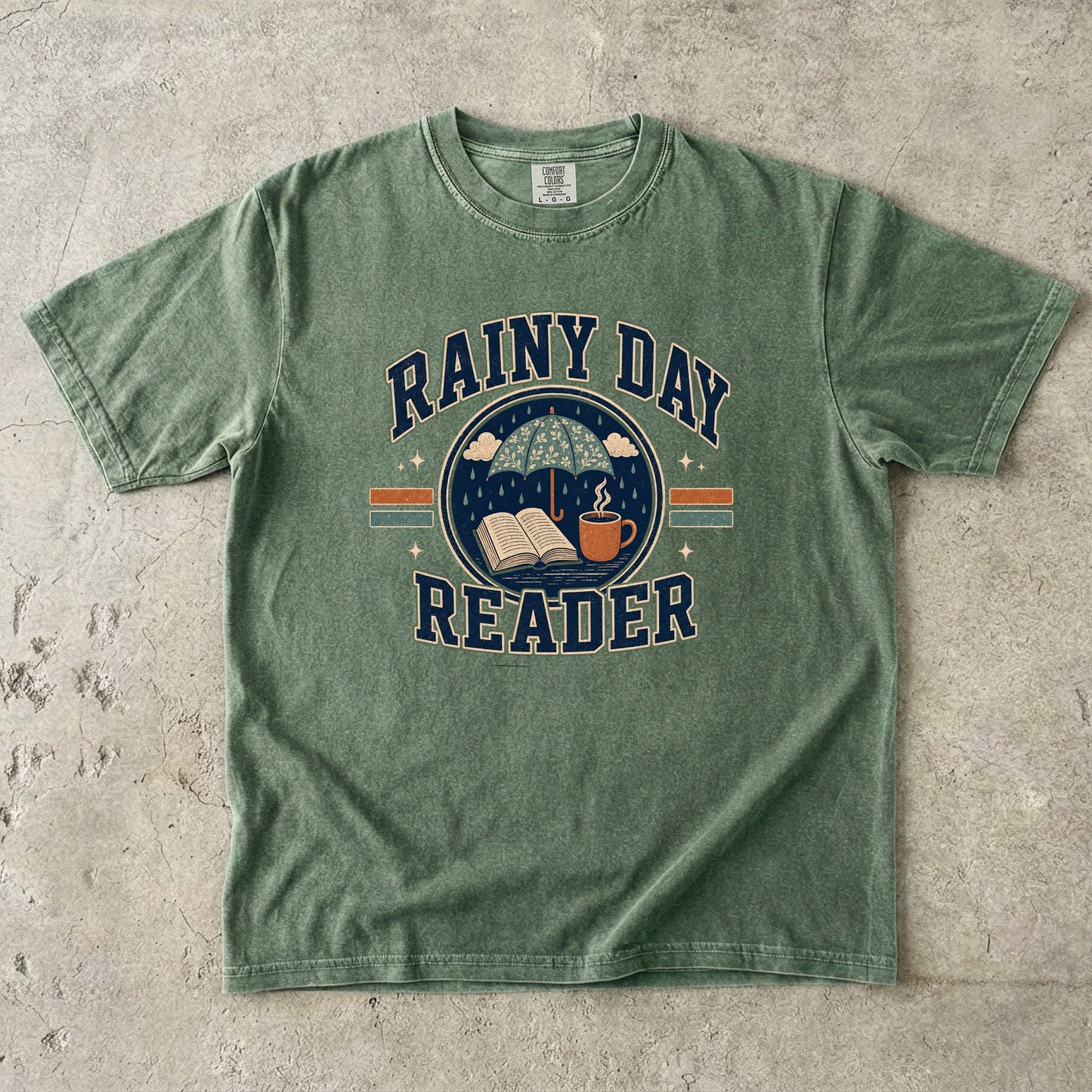 Ivory Comfort Colors Rainy Day Reader T-shirt featuring a vintage umbrella, open book and warm drink illustration.