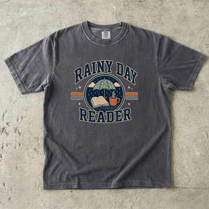 Pepper Comfort Colors Rainy Day Reader T-shirt with a vintage book, umbrella, rain and warm drink graphic.