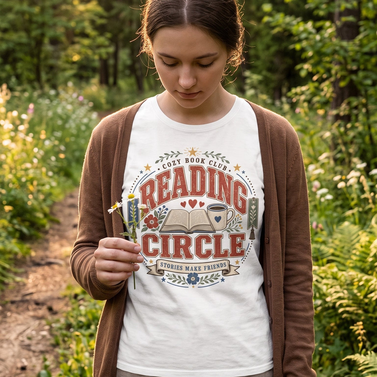 Woman wearing the Reading Circle cozy book club T-shirt outdoors, featuring an open book, coffee mug, flowers and Stories Make Friends design.