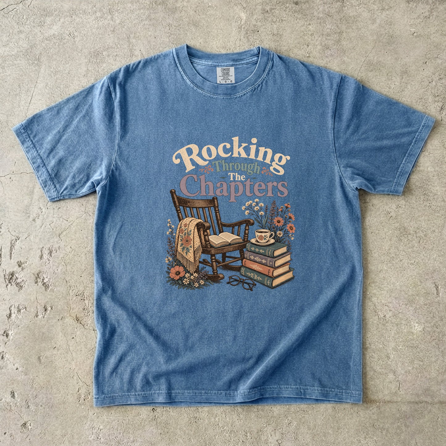 Rocking Through the Chapters cozy reading T-shirt in Blue Jean featuring a vintage rocking chair, open book, stacked books and teacup