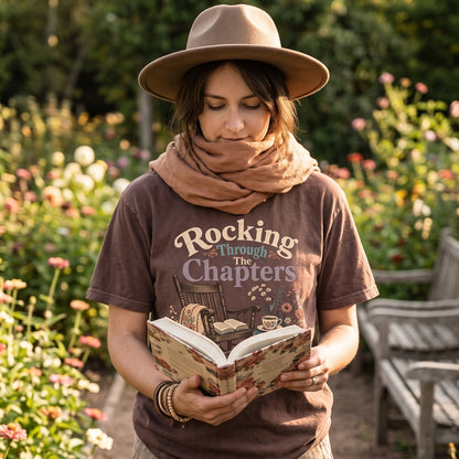 Rocking Through the Chapters cozy reading T-shirt featuring a rocking chair, open book, floral blanket, stacked books, teacup and flowers