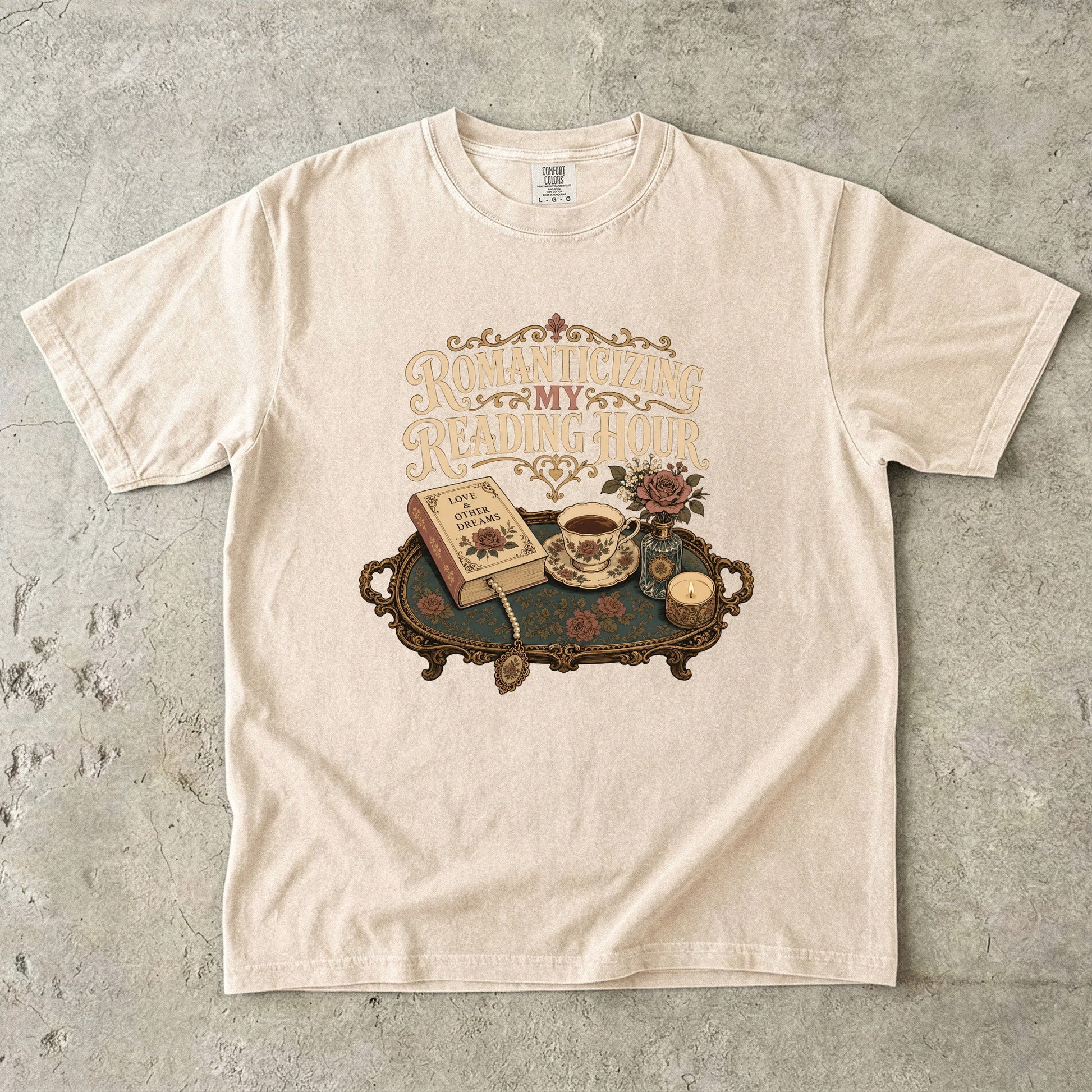 front view of an Ivory Comfort Colors® book lover T-shirt featuring the Romanticizing My Reading Hour vintage reading illustration with a romance novel, teacup, candle and floral accents.