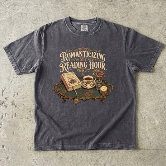 Front view of a Pepper Comfort Colors® book lover T-shirt featuring the Romanticizing My Reading Hour vintage design with a romance novel, teacup, candle, floral arrangement and decorative tray.