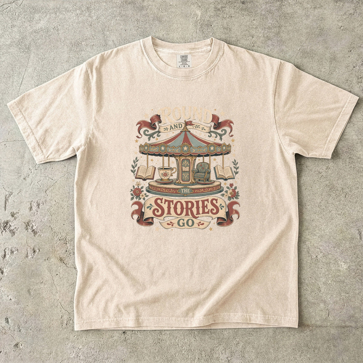 Round and Round the Stories Go book lover T-shirt in Ivory featuring a vintage carousel with open books, reading chair and teacup