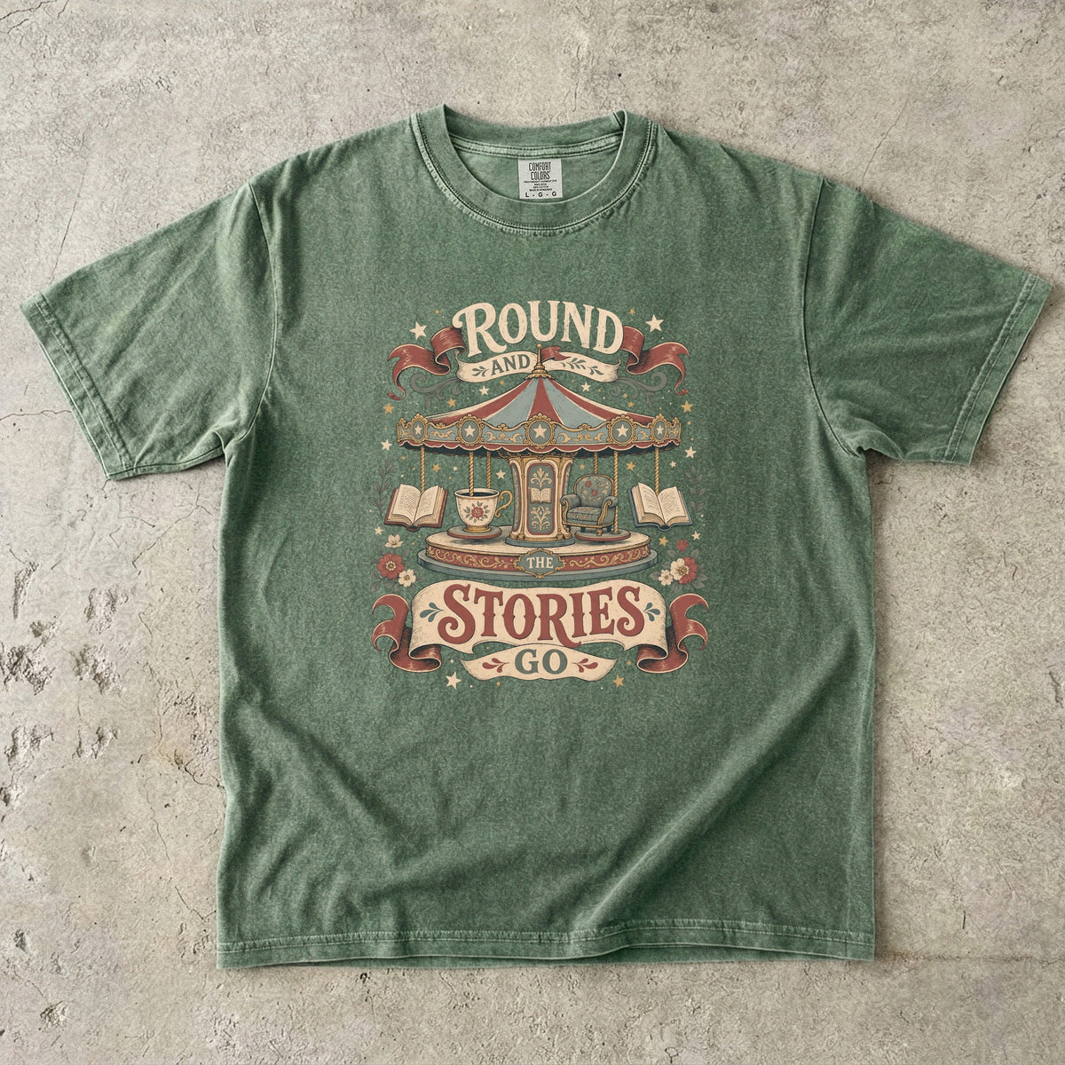Round and Round the Stories Go book lover T-shirt in Moss featuring a vintage carousel with open books, reading chair and teacup