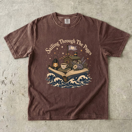 Front view of a Expresso Comfort Colors® Book Lover T-shirt featuring the "Sailing Through the Pages" vintage literary illustration with an open book boat, waves, lantern and cozy cottage.