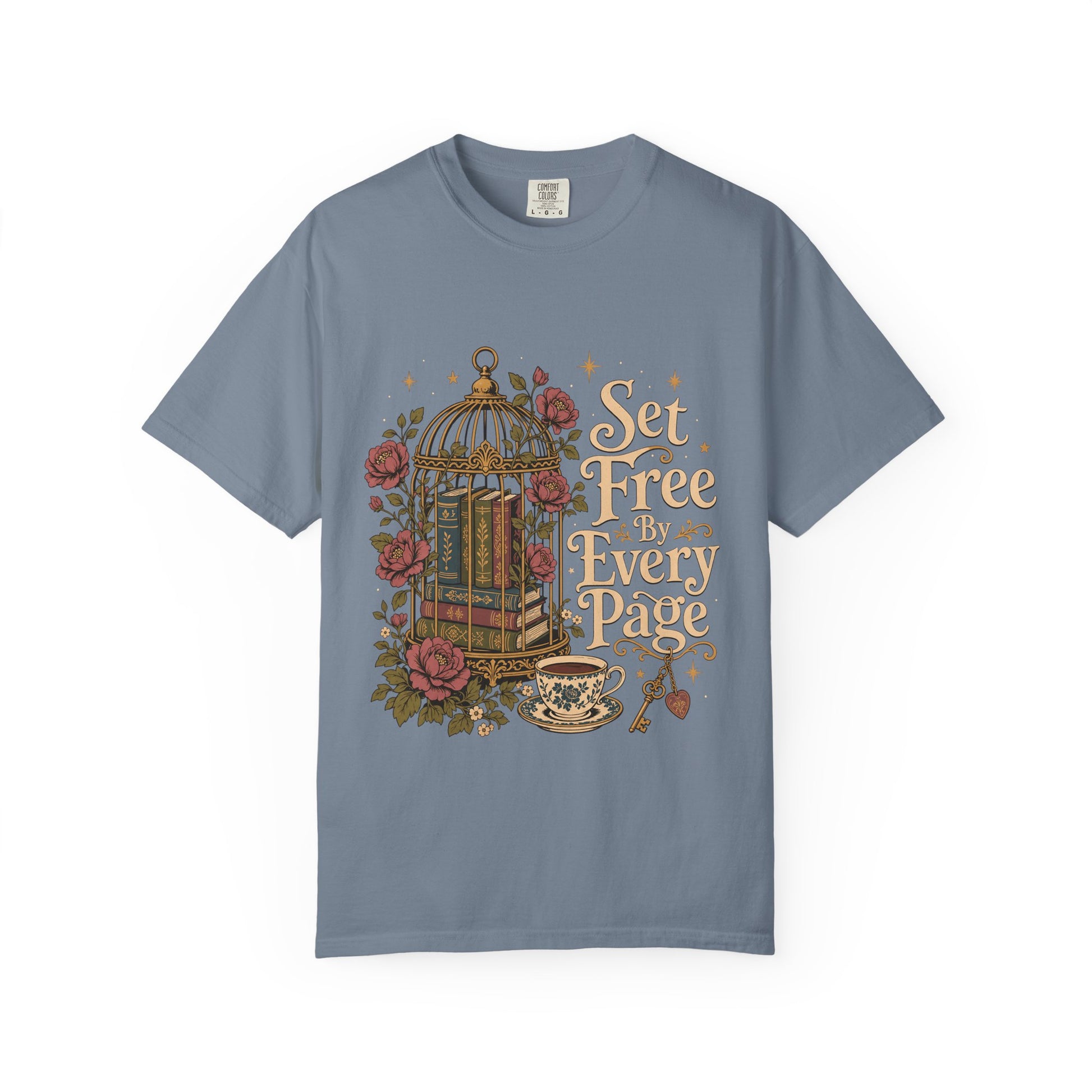 Front view of a Blue Jean Comfort Colors book lover T-shirt featuring the vintage "Set Free By Every Page" illustration with a decorative birdcage, antique books, blooming roses, teacup and ornate key.