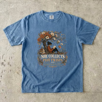 Blue Jean reading T-shirt featuring She Collects Plot Twists and Paperbacks with a reader beneath a flowering tree surrounded by books.