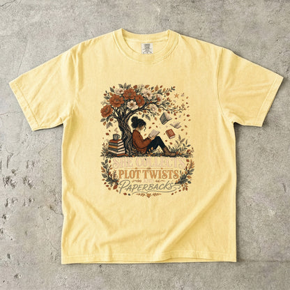 Butter reading T-shirt featuring She Collects Plot Twists and Paperbacks with a reader beneath a flowering tree surrounded by books.